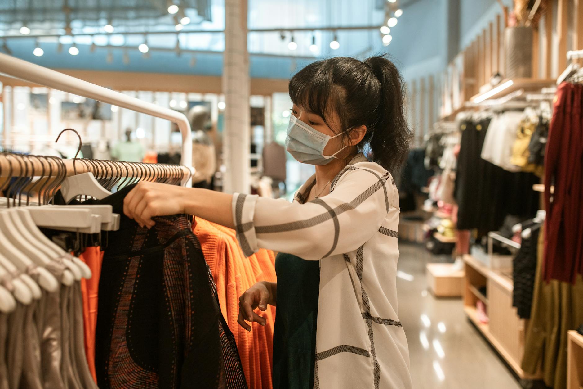 Woman wearing a face mask shopping for clothes in a department store.