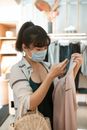 一位女子在一家现代商店里检查衣服，她戴着口罩