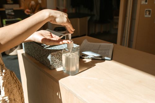 Free Close-up of a person using hand sanitizer at a desk, highlighting hygiene during daylight indoors. Stock Photo