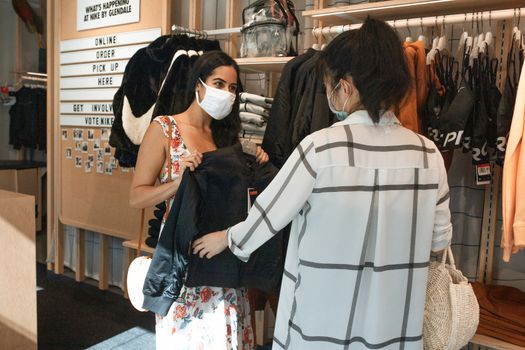 两名戴着口罩的妇女正在一家时尚精品店购买夹克