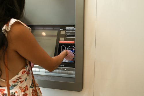 Femme En Robe à Fleurs Rouge Blanc Et Vert Debout Près De La Machine Atm