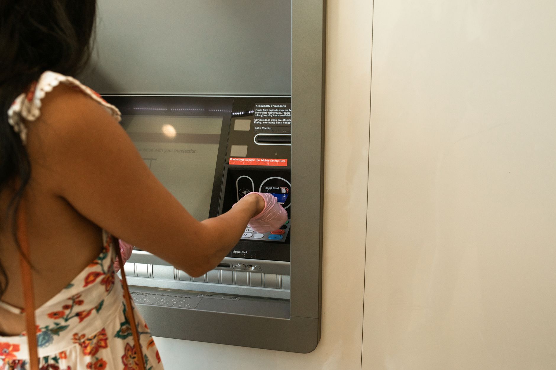 Woman using an ATM machine while wearing protective gloves indoors.