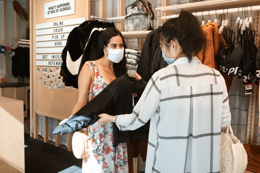 两名戴着口罩的妇女正在一家服装店买夹克