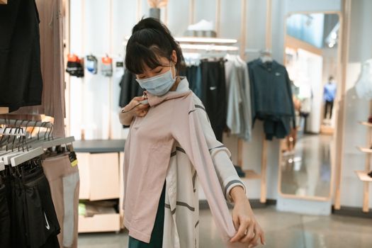 一名女子戴着口罩在精品店试穿粉色上衣，展现了时尚潮流
