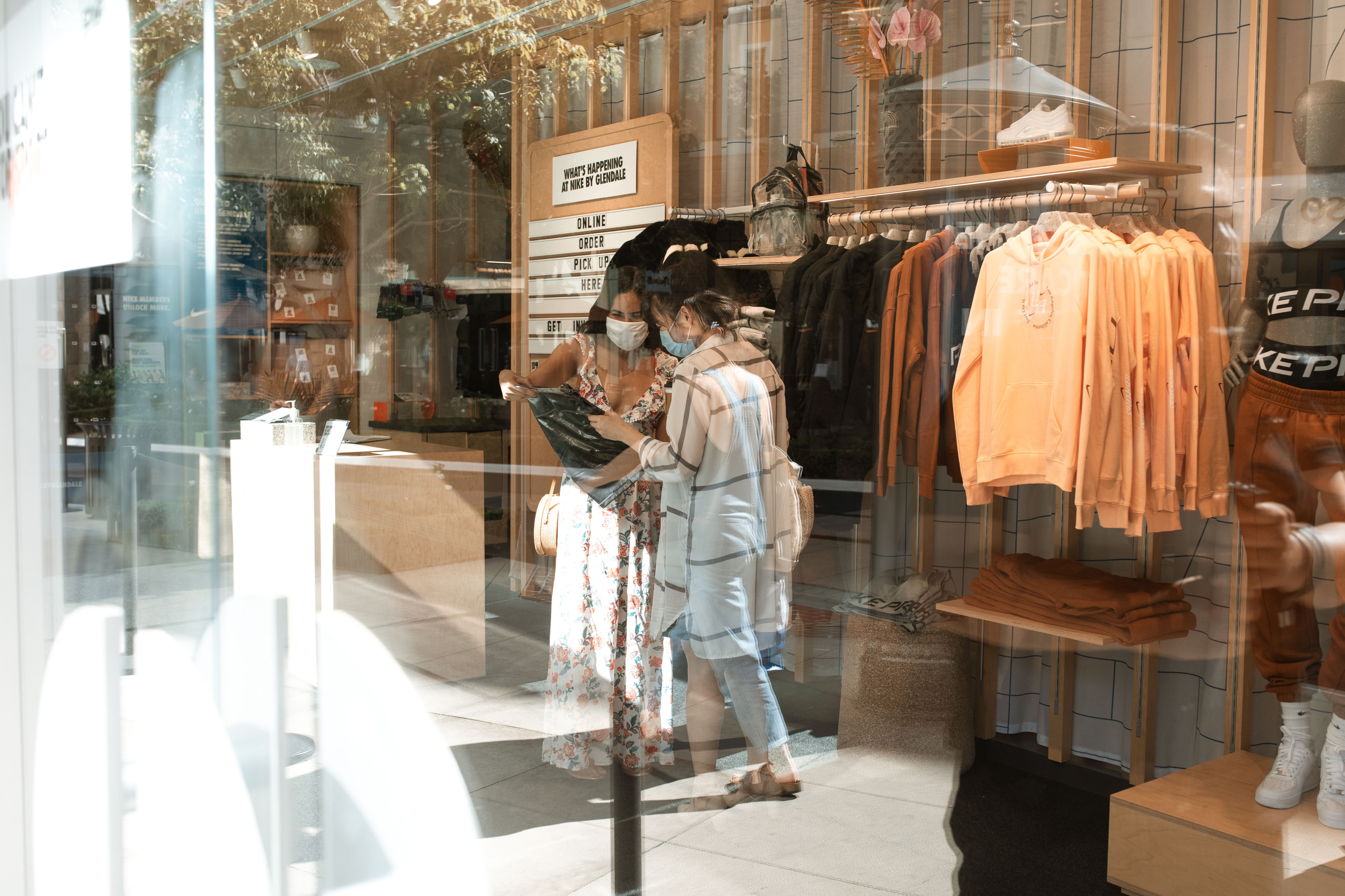 两名妇女戴着口罩，在一家时尚精品店购物，采取了疫情预防措施