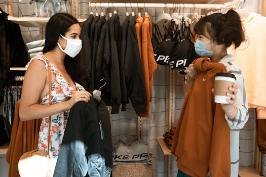 Two women wearing masks shop for jackets, illustrating the new normal.