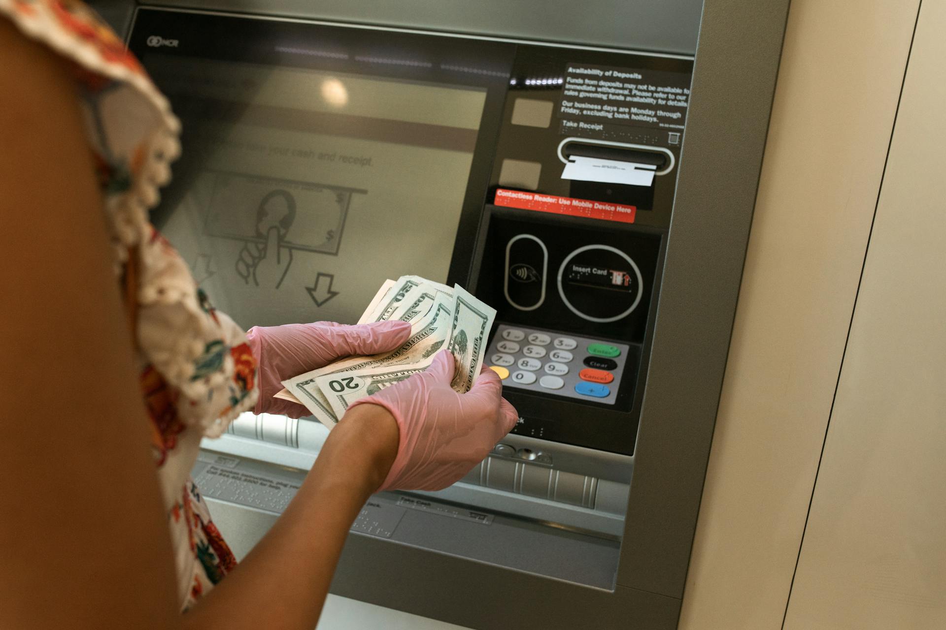 A person wearing gloves withdraws cash from an ATM, ensuring hygiene.