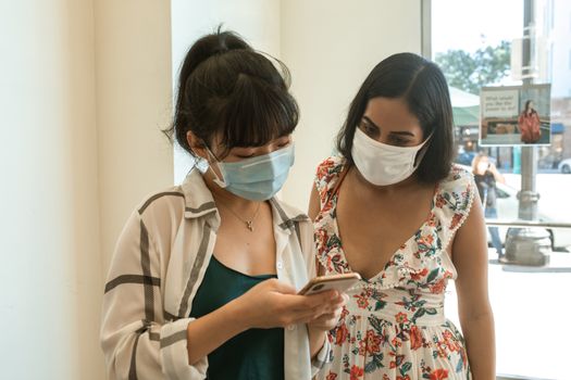 两名女士戴着口罩，在室内专注地使用智能手机