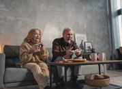 一对老年夫妇在客厅的沙发上愉快地玩着电子游戏，享受着室内有趣而放松的时光