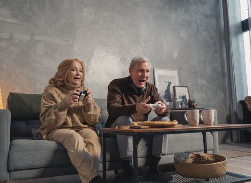 Free Senior couple happily playing video games on the couch at home, enjoying a fun and relaxing time indoors. Stock Photo