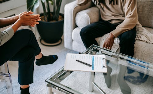 Free Crop anonymous African American man in casual clothes sitting on sofa and talking to female psychologist during psychotherapy session in modern studio Stock Photo