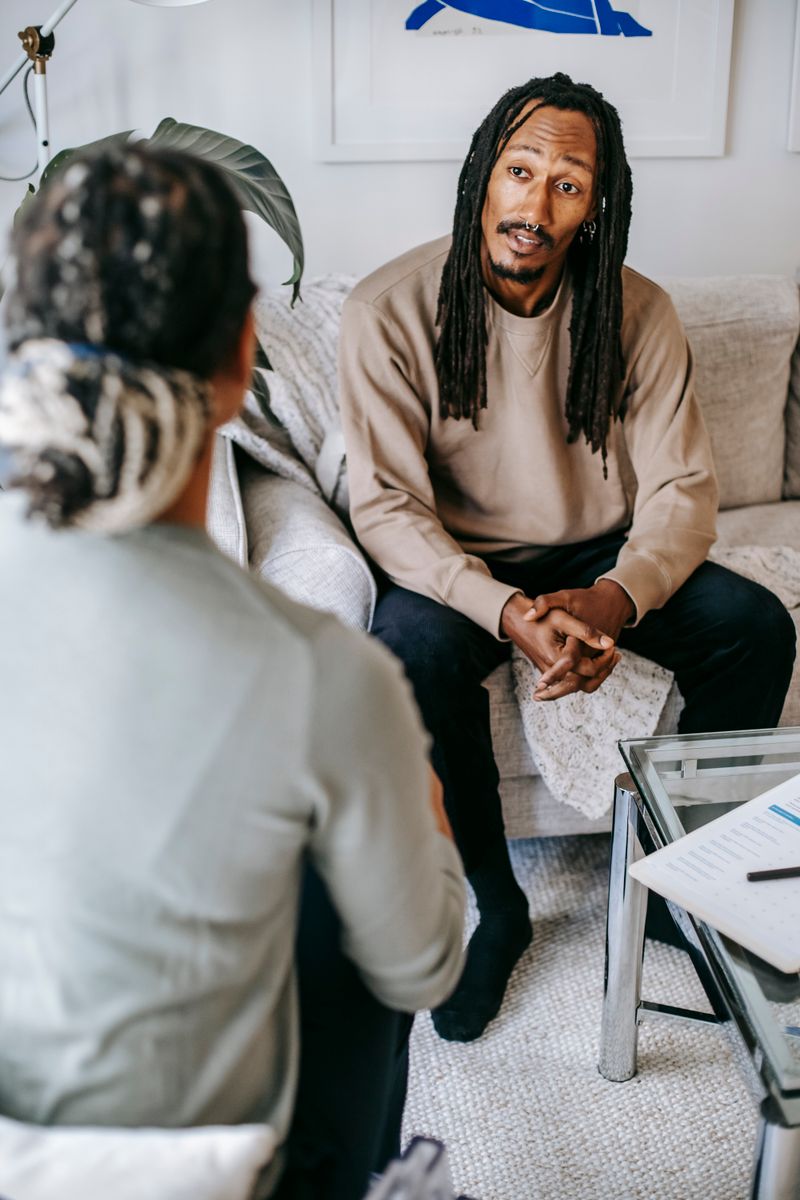 A Black man sits across from a female psychologist during a counseling session, both engaged and calm.