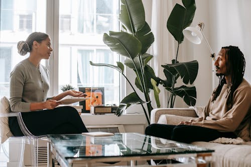 Free Side view of professional female African American therapist sitting in front of black male patient during psychotherapy session in office Stock Photo