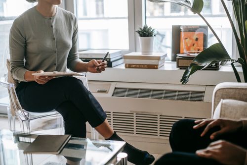 Free Unrecognizable female psychologist with crossed legs writing information on clipboard during appointment with anonymous ethnic patient in cozy light office Stock Photo