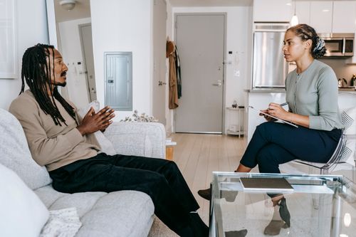 Free Side view of African American female therapist with crossed legs and clipboard taking notes while sitting in front of black male patient Stock Photo