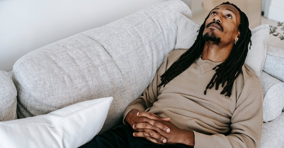 Man with dreadlocks lies on couch, looking up, expressing contemplation and introspection indoors.