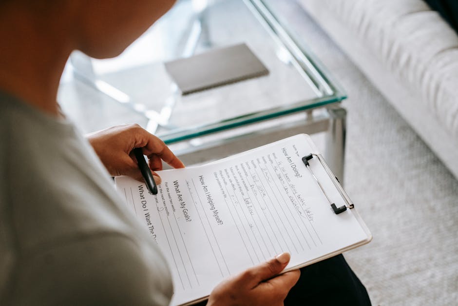 From above of blurred anonymous female psychologist reading documents on clipboard while sitting in office near table during session