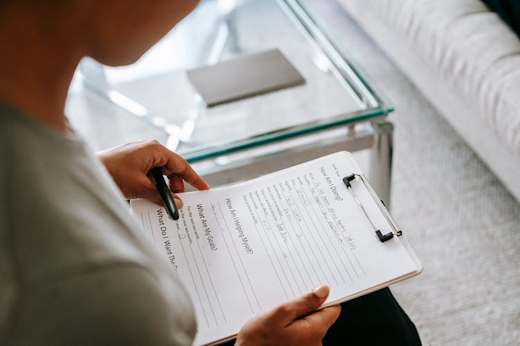 Crop Woman Reading Notes On Clipboard