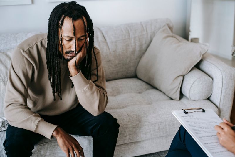 A Black man sits with his hand to his face during a counseling session as a therapist takes notes on an intake form. PTSD is treatable, and trauma-focused therapy works.