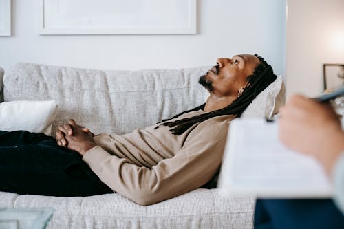 Side view of thoughtful African American male with beard and mustache relaxing and dreaming on sofa in lounge