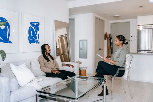 Free Concerned African American male in smart casual clothes sitting on comfortable sofa and sharing problems with empathetic female consultant in contemporary psychotherapy center Stock Photo