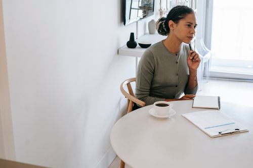 Free Concentrated ethnic female HR interviewer or psychologist in formal clothes sitting at round table with pen and notepad while looking away in contemplation Stock Photo