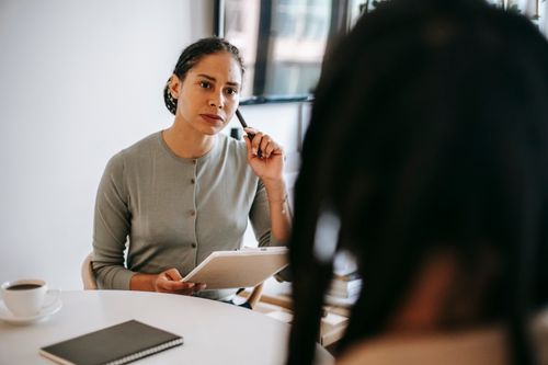 Free Focused ethnic female counselor in formal wear with clipboard and pen listening to patient problems during psychotherapy session Stock Photo