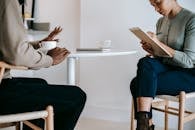 Crop ethnic female psychotherapist in formal clothes writing notes in clipboard while listening to black male patient complains in light studio