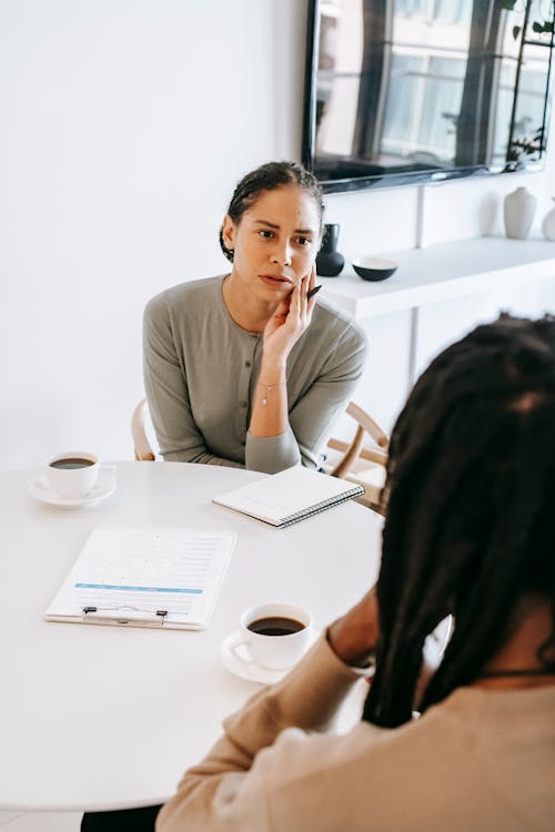 Free Serious ethnic female consultant listening to black male client problems while sitting at round table together in light psychology center Stock Photo