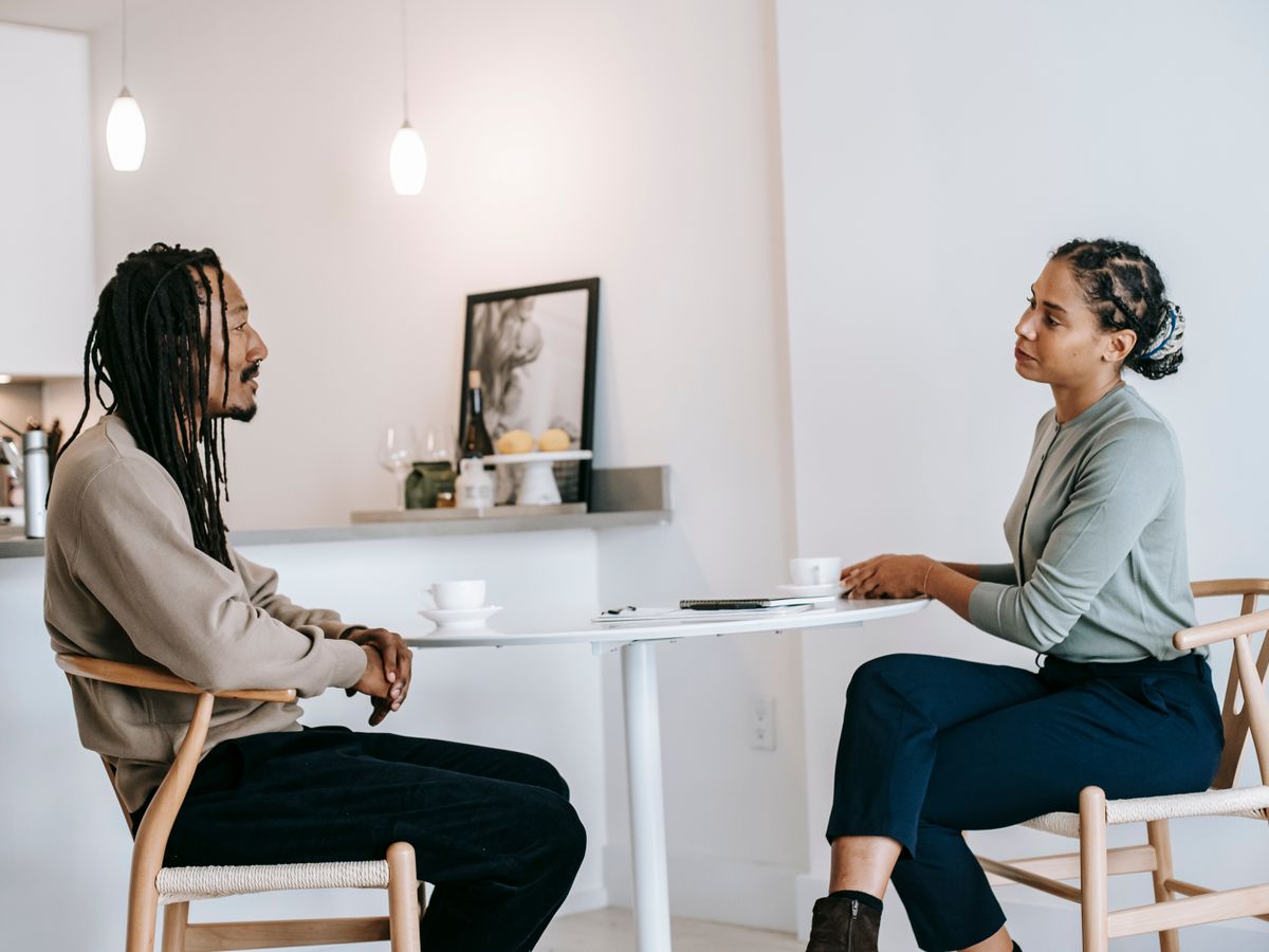 A person speaking quietly while another listens with a notebook, in a calm room.