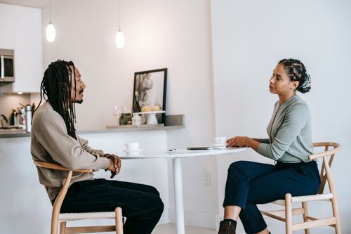 Free Side view adult African American male in smart casual with dreadlocks answering professional female psychotherapist questions during psychotherapy in light studio Stock Photo