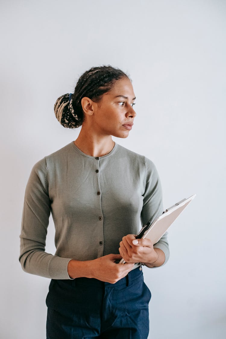 Focused Ethnic Woman With Clipboard Standing Against White Wall