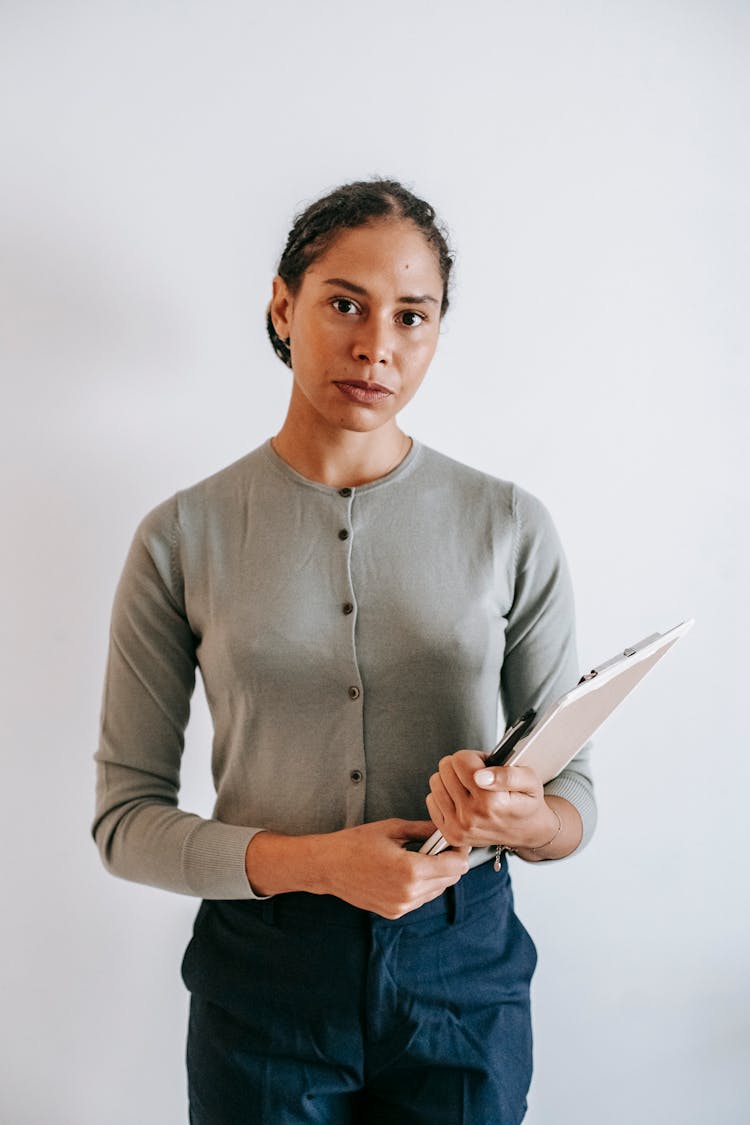 Calm Female With Clipboard Standing Against White Wall