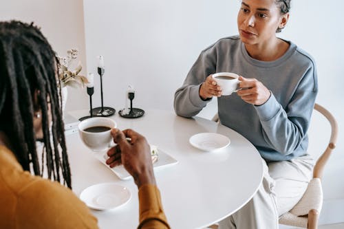 Free From above of crop pensive Hispanic female in casual clothes sitting at light table and drinking coffee with African American boyfriend in modern cafe Stock Photo