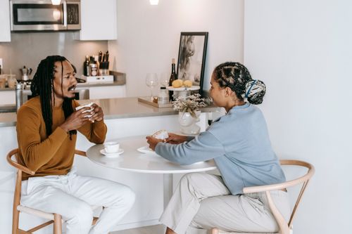Free Positive diverse couple in casual clothes sitting at table with cup of drink and eating delicious food while spending time together in kitchen at home Stock Photo