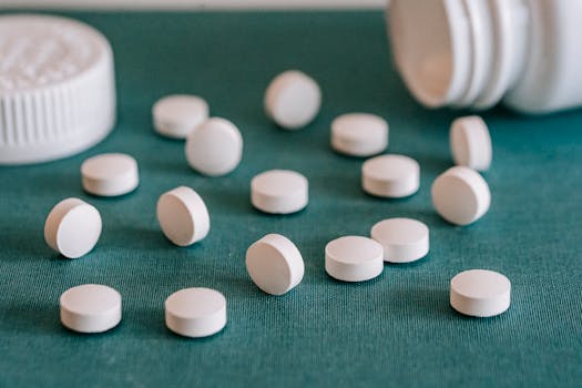 Close-up of white pills spilled from a container on a textured green surface.