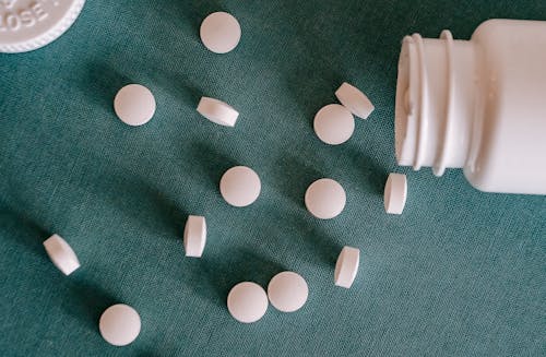Top view of similar small round white pills spilled from plastic container on green surface