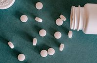 从塑料容器中溢出到绿色表面的类似小圆白色药丸的顶视图
