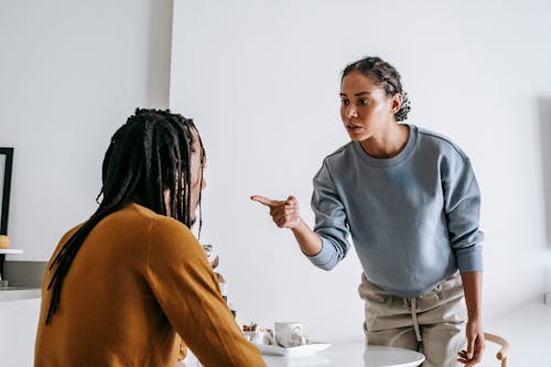 Young African American female standing near table while male sitting at kitchen and having argument