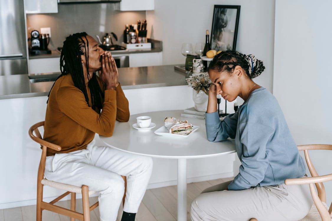 Free Young African American man sitting at table with woman and looking down thoughtfully while having conflict Stock Photo