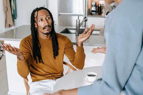 Free Black male sitting at table and arguing with standing near table female in casual outfit in light kitchen Stock Photo