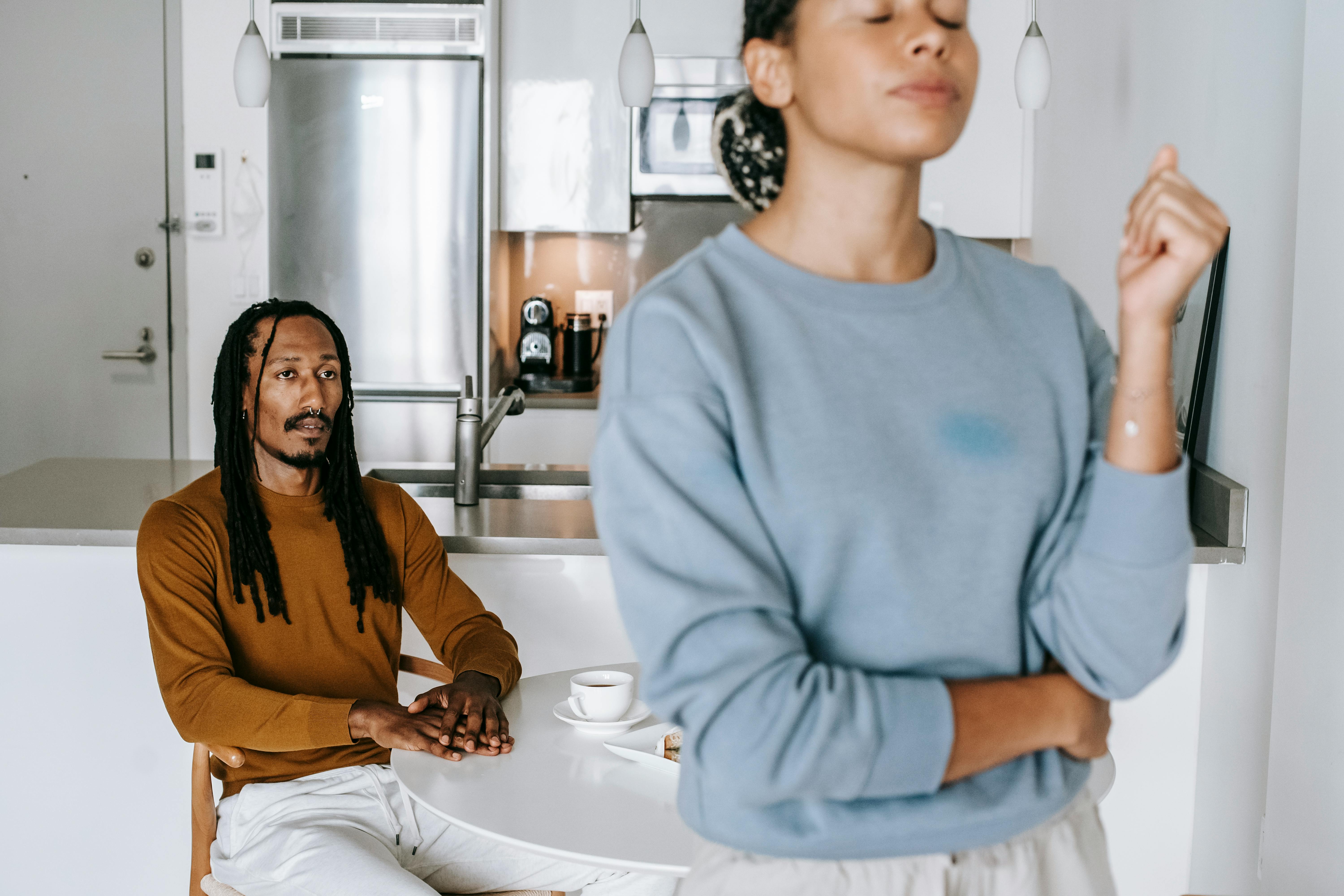 Kitchen scene showing relationship tension with a woman in the foreground looking away while a man sits at the counter in the background, illustrating the emotional distance created by narcissist manipulation tactic