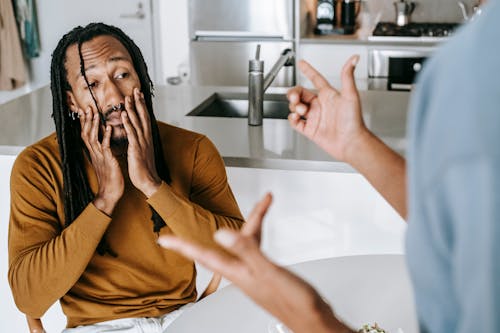 Free Young African American male sitting at table with hands on face and having conflict with female on kitchen Stock Photo