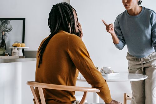 Free Young African American lady standing near table while having argument with guy sitting at kitchen Stock Photo