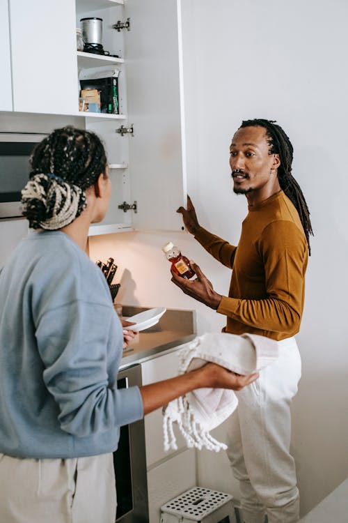 Black man and woman arguing and talking in kitchen while standing near shelves in daytime