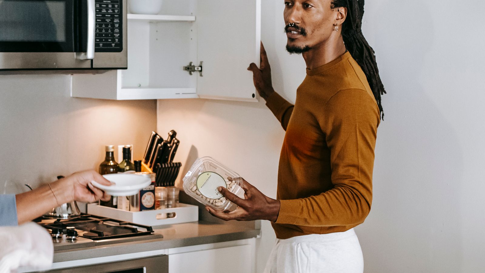 Two people holding food containers beside an open kitchen cupboard