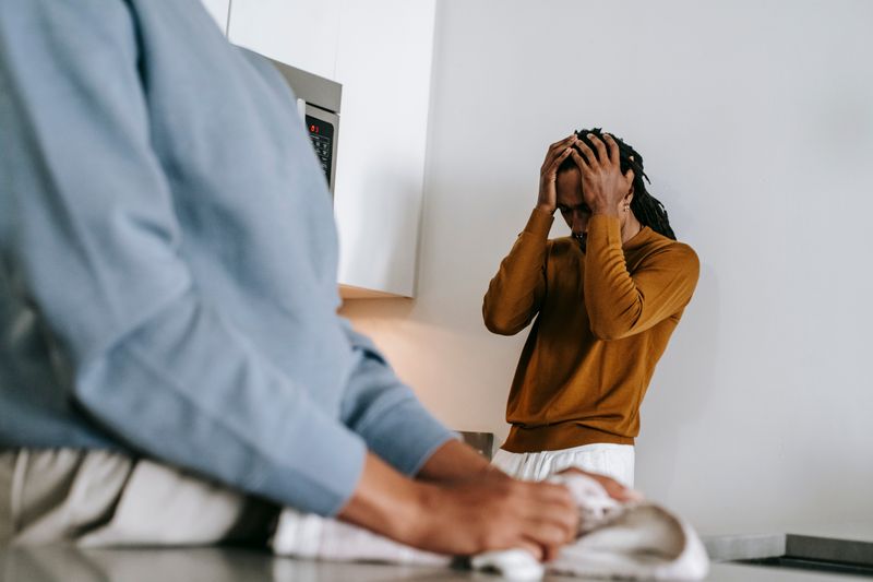 Black man and faceless woman arguing while standing in kitchen and wearing casual clothes in daytime