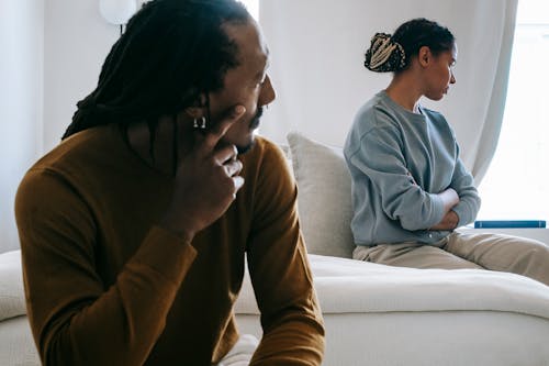 Free Young African American couple sitting on bed with sad face in casual outfit and thinking at home Stock Photo