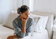 一位年轻女子若有所思地坐在现代宁静的卧室床上