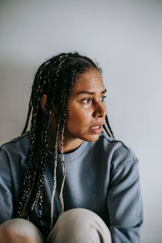 一位扎着非洲辫子、穿着休闲服装的年轻非裔美国女性，在白天悲伤地看向别处